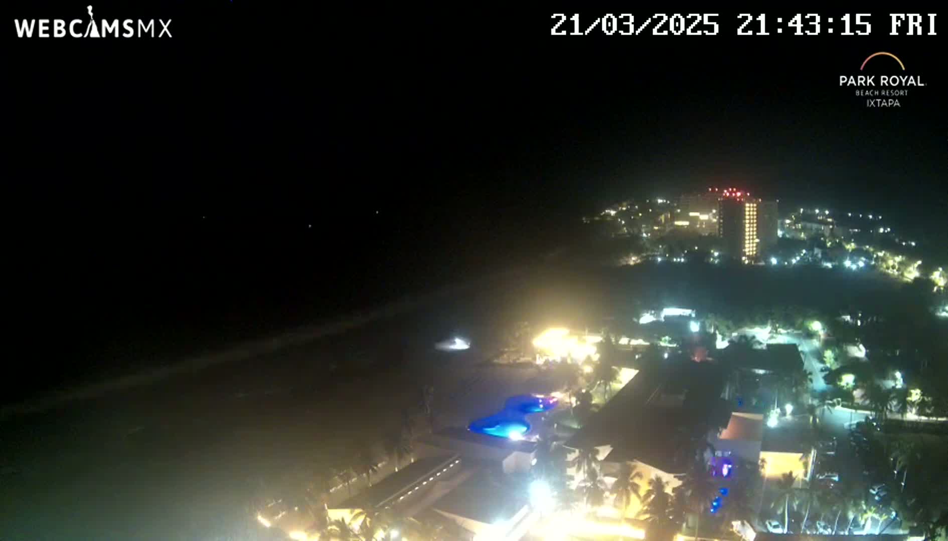 A nighttime, high-angle view shows a resort town illuminated along a dark ocean shore under a clear sky.