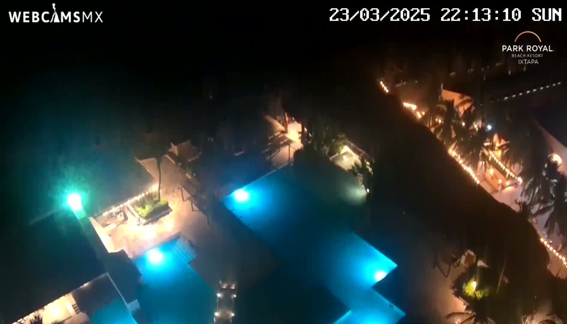 An aerial nighttime view shows a resort with illuminated swimming pools and landscaping under a clear sky.