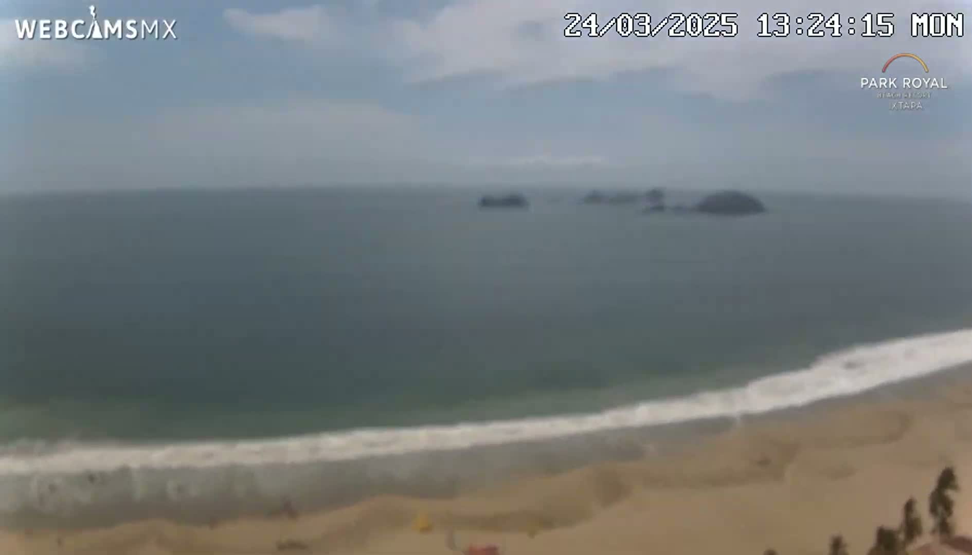 A mostly cloudy day shows an ocean beach scene with small waves breaking on the shore and several small islands visible in the distance.