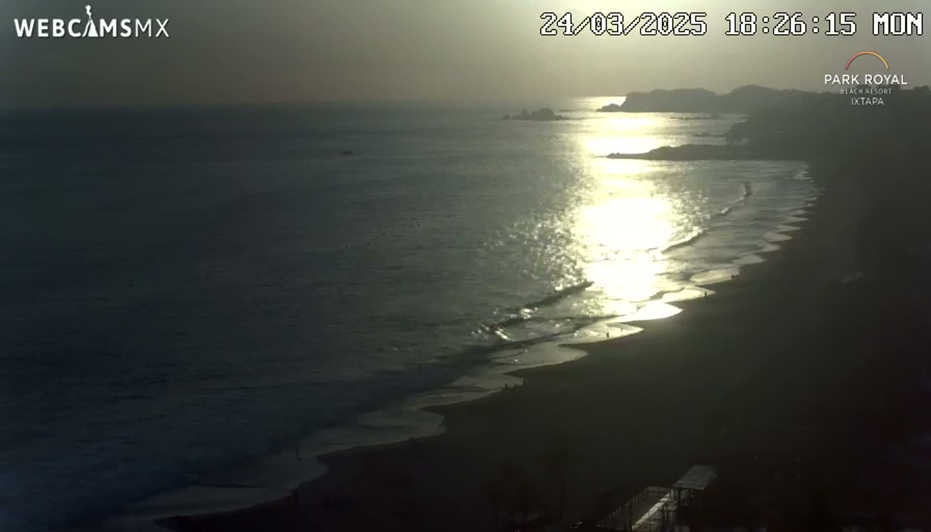 A beach at sunset, with calm waves gently lapping the shore and the sun reflecting on the water.