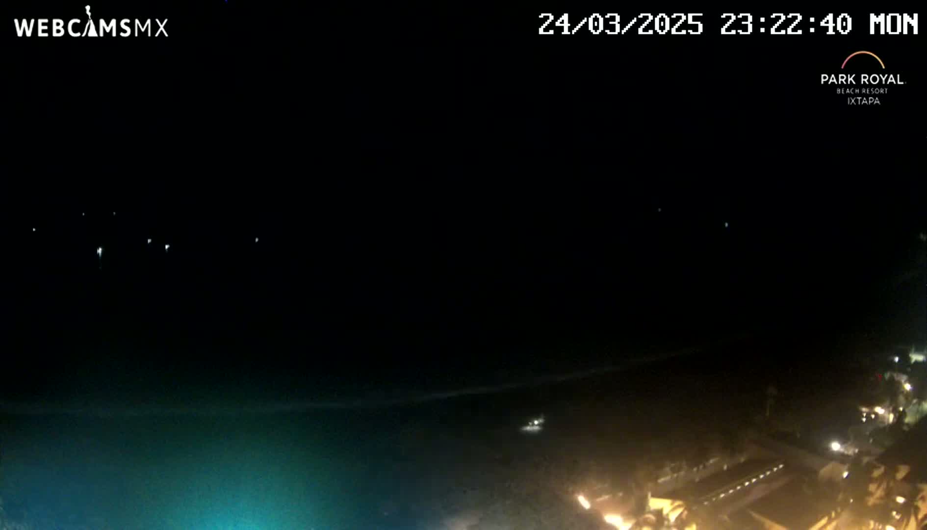 A nighttime view of a dark ocean, with a few distant lights visible on the water and more lights closer to the shoreline at the bottom of the frame.