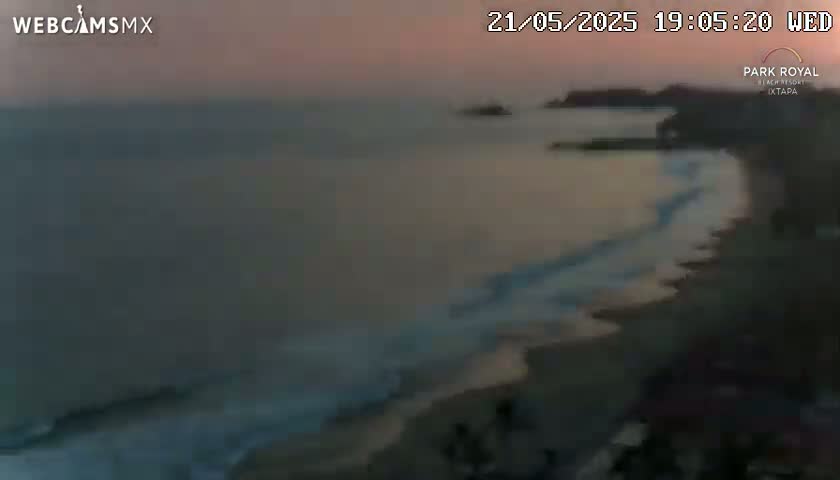 A beach at sunset shows gentle waves lapping the shore under a dusky sky.