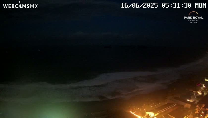 A nighttime coastal scene shows dark, slightly wavy ocean meeting a dimly lit shoreline with buildings and lights.