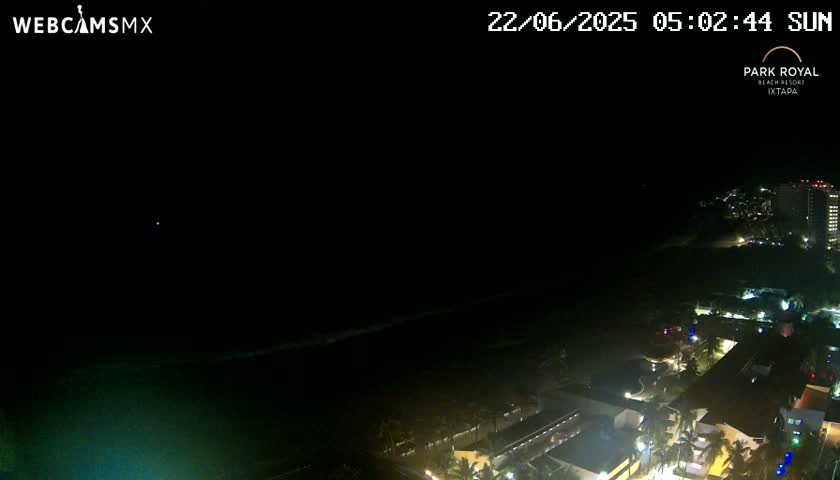 A nighttime, high-angle view shows a dark ocean and a dimly lit resort area.