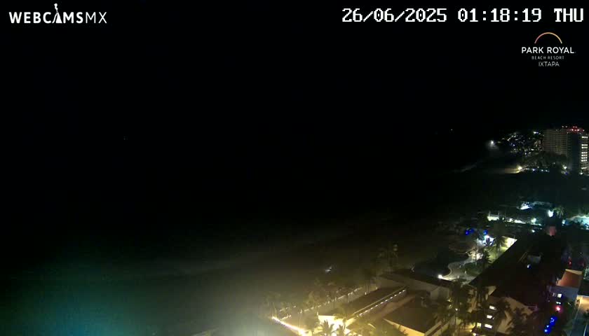 A nighttime, high-angle view shows a dark ocean, a dimly lit beach, and illuminated buildings along a coastline.
