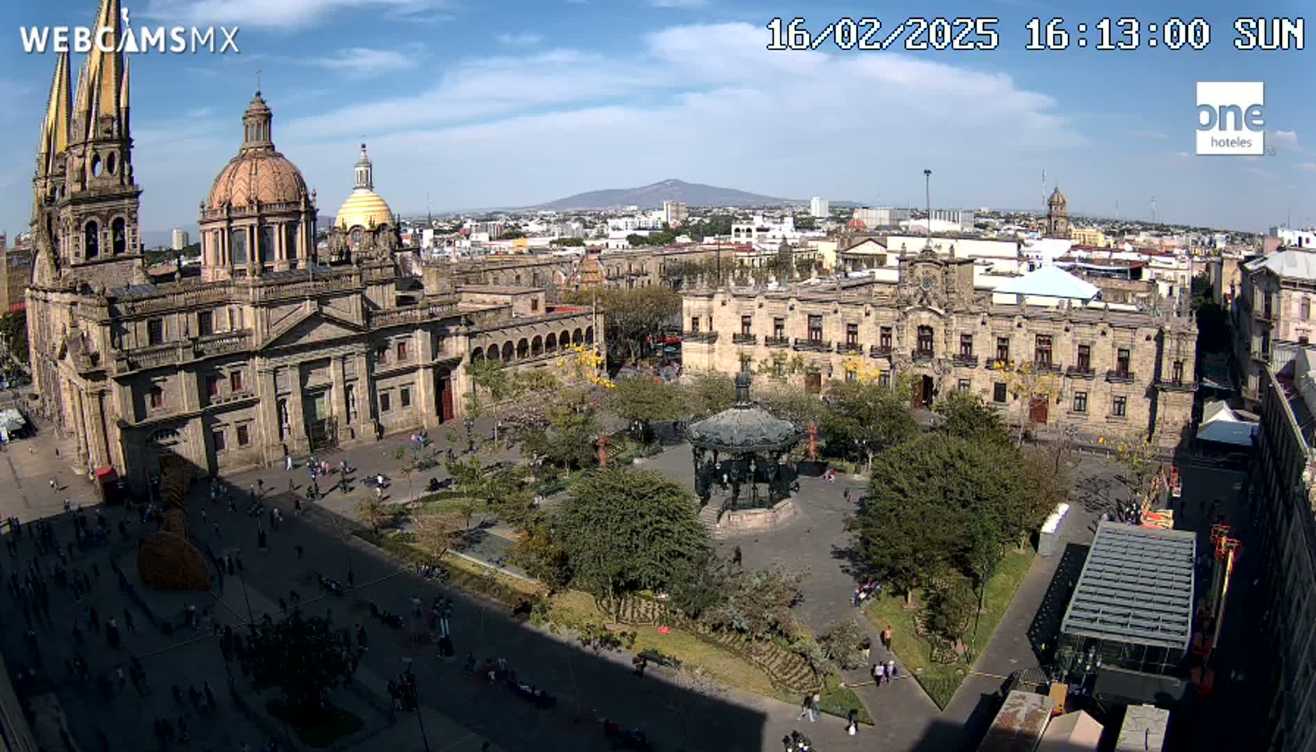 A large plaza with a cathedral, government buildings, and a gazebo is shown under sunny skies, with a distant mountain visible in the background.