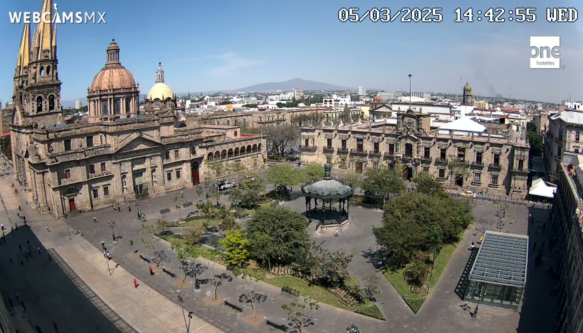 A large plaza with a gazebo, surrounded by historic buildings including a cathedral, under a clear, sunny sky.