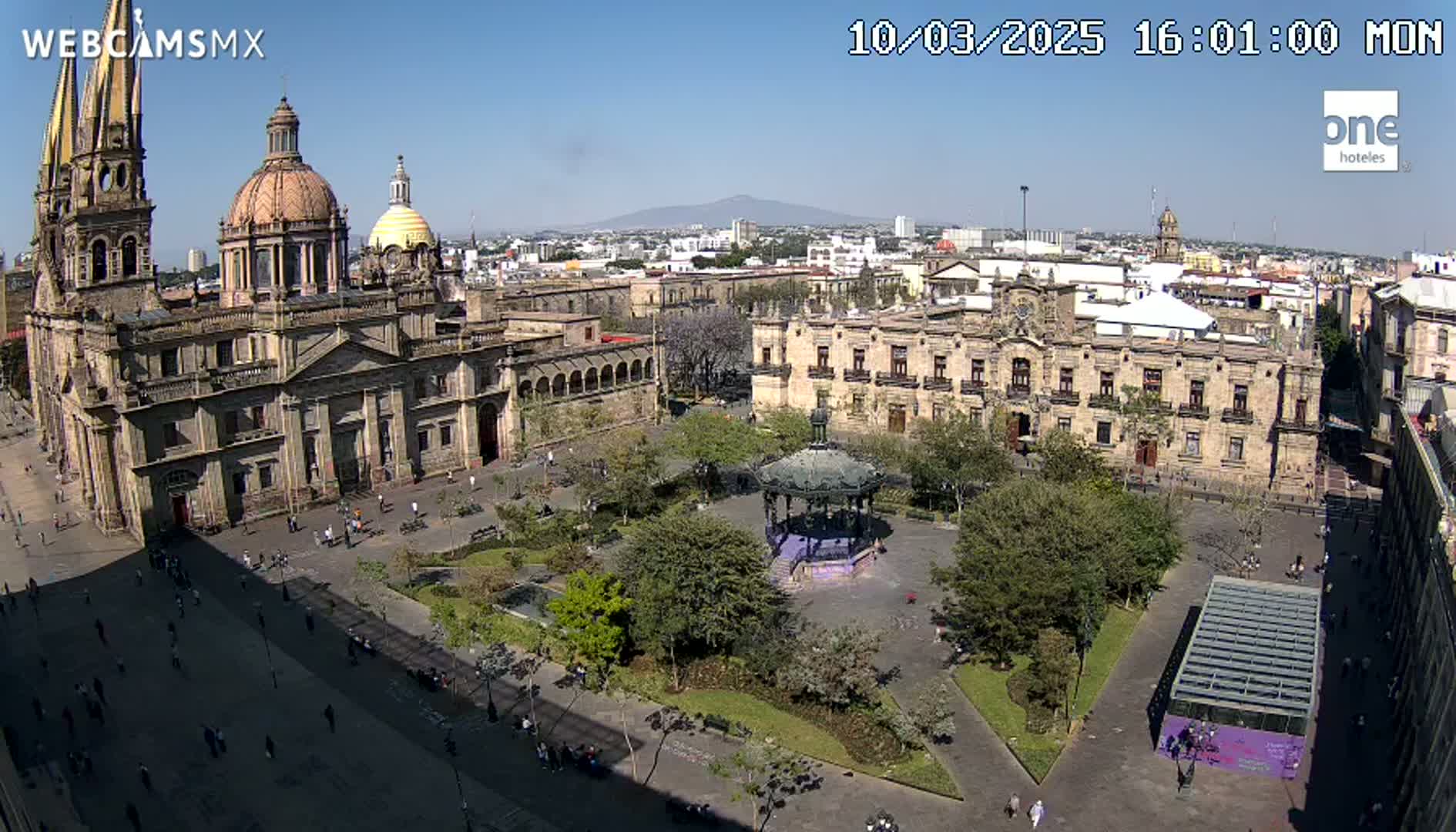 A large plaza with a cathedral and government buildings is seen on a sunny day, with a distant mountain visible in the background.