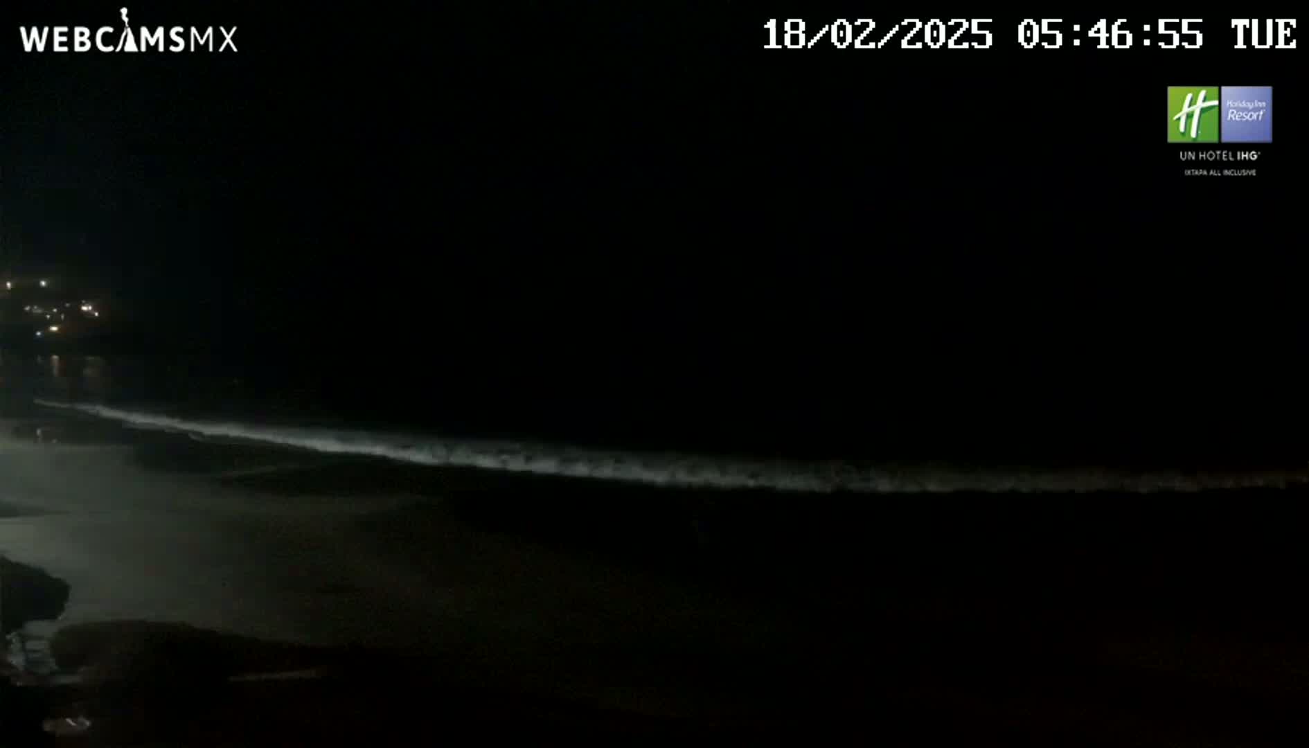 A dark nighttime beach scene shows gently lapping waves under a clear, starless sky.
