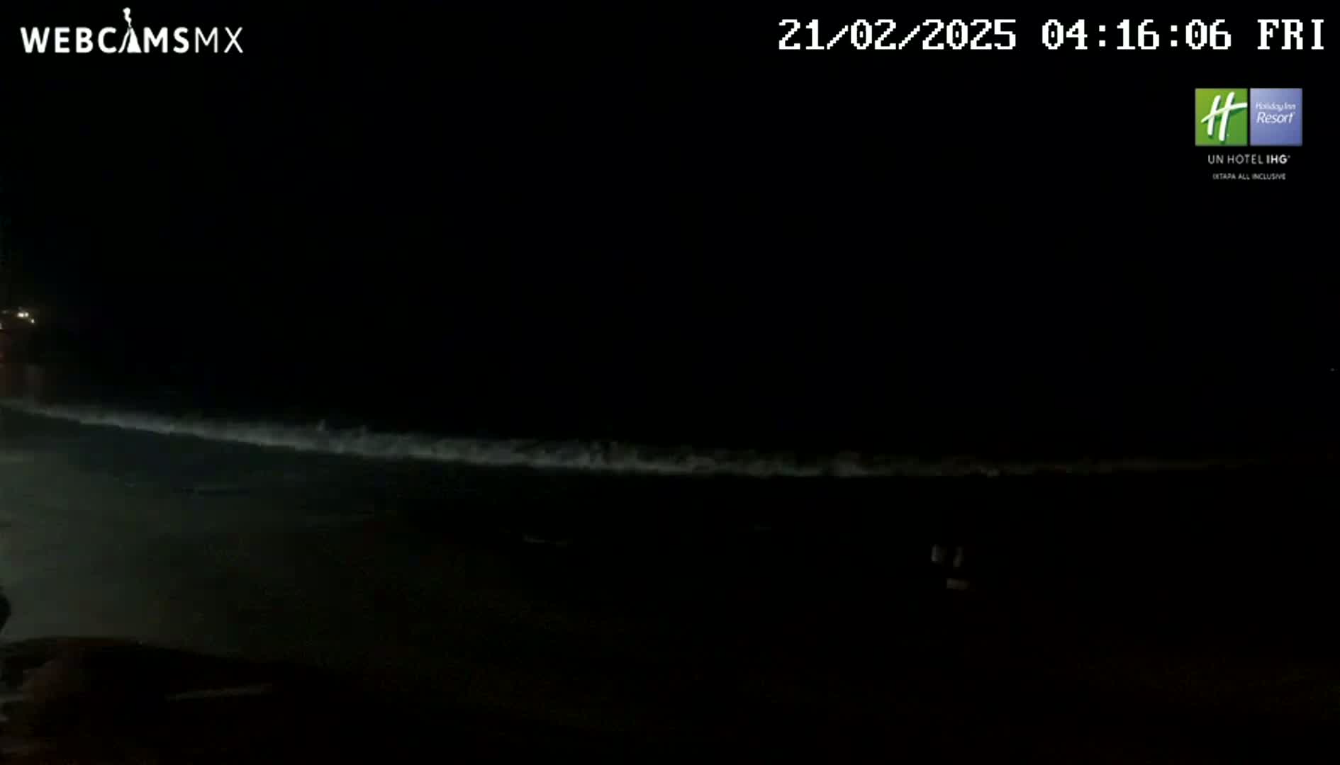 A dark, nighttime beach scene shows gently rolling waves under a clear, black sky.