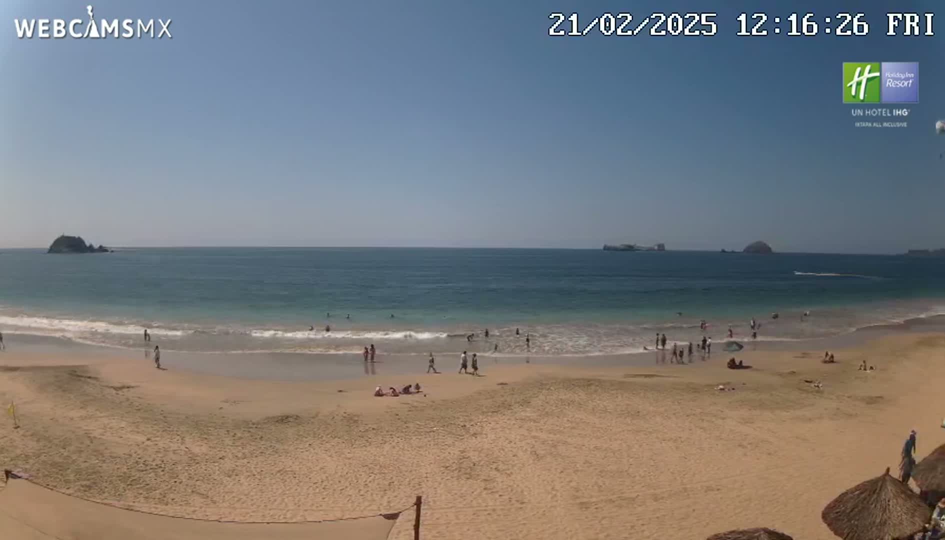 A sandy beach with a calm ocean and several people enjoying the sunny day.