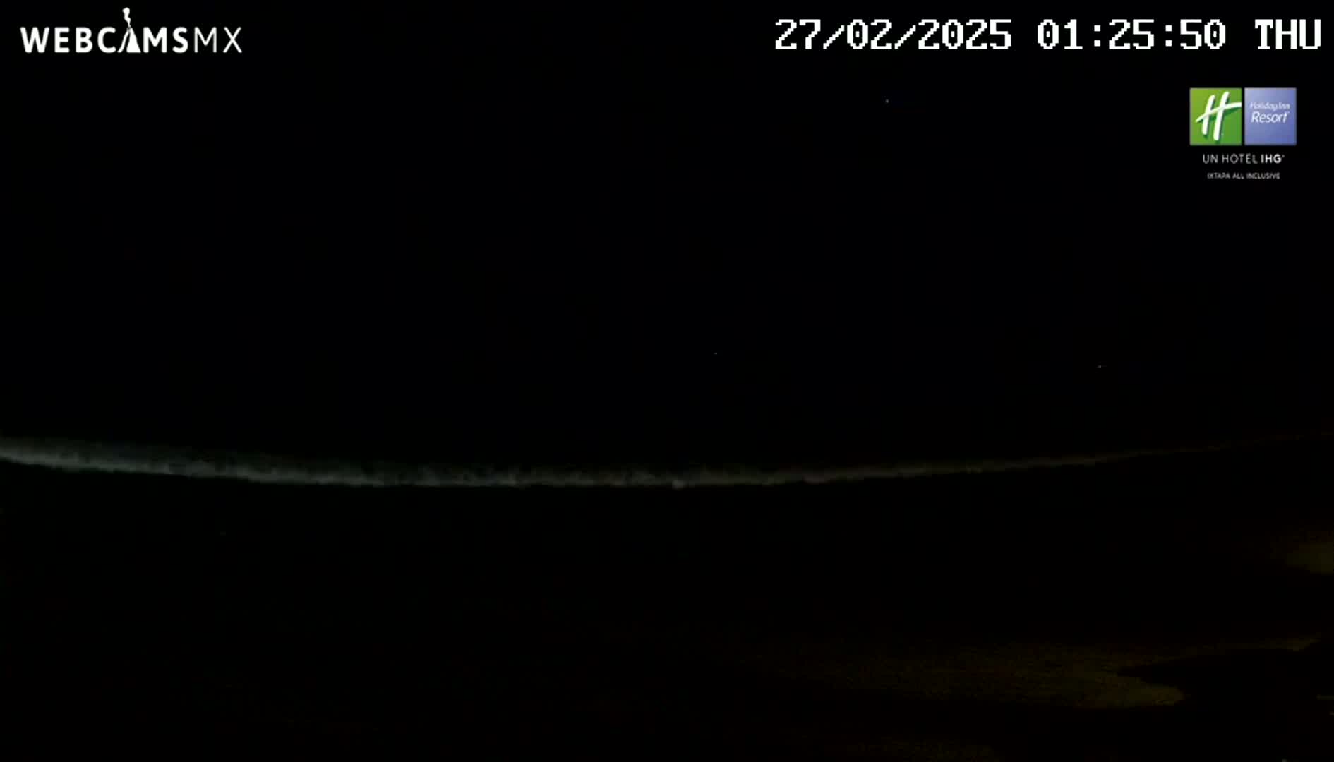 A nighttime ocean scene shows a faint, bright line on the horizon under a dark sky.