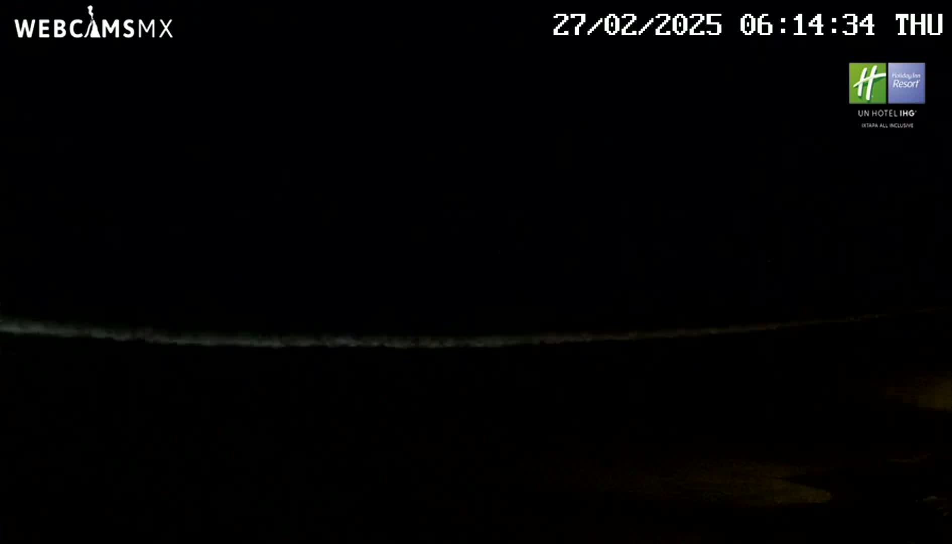 A dark nighttime scene shows a faintly illuminated horizon line, possibly the ocean, under a mostly clear sky.