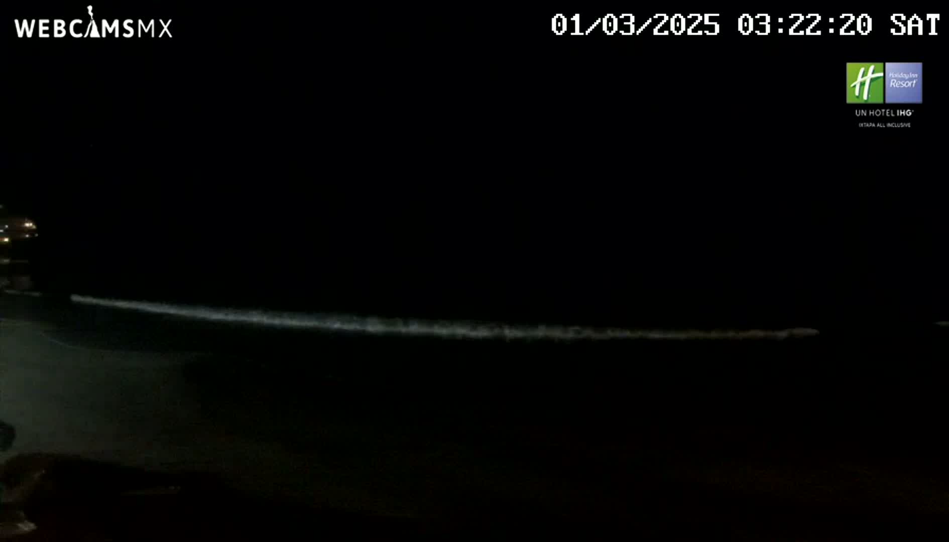 A nighttime beach scene shows a faint line of waves breaking on the shore under a dark sky.