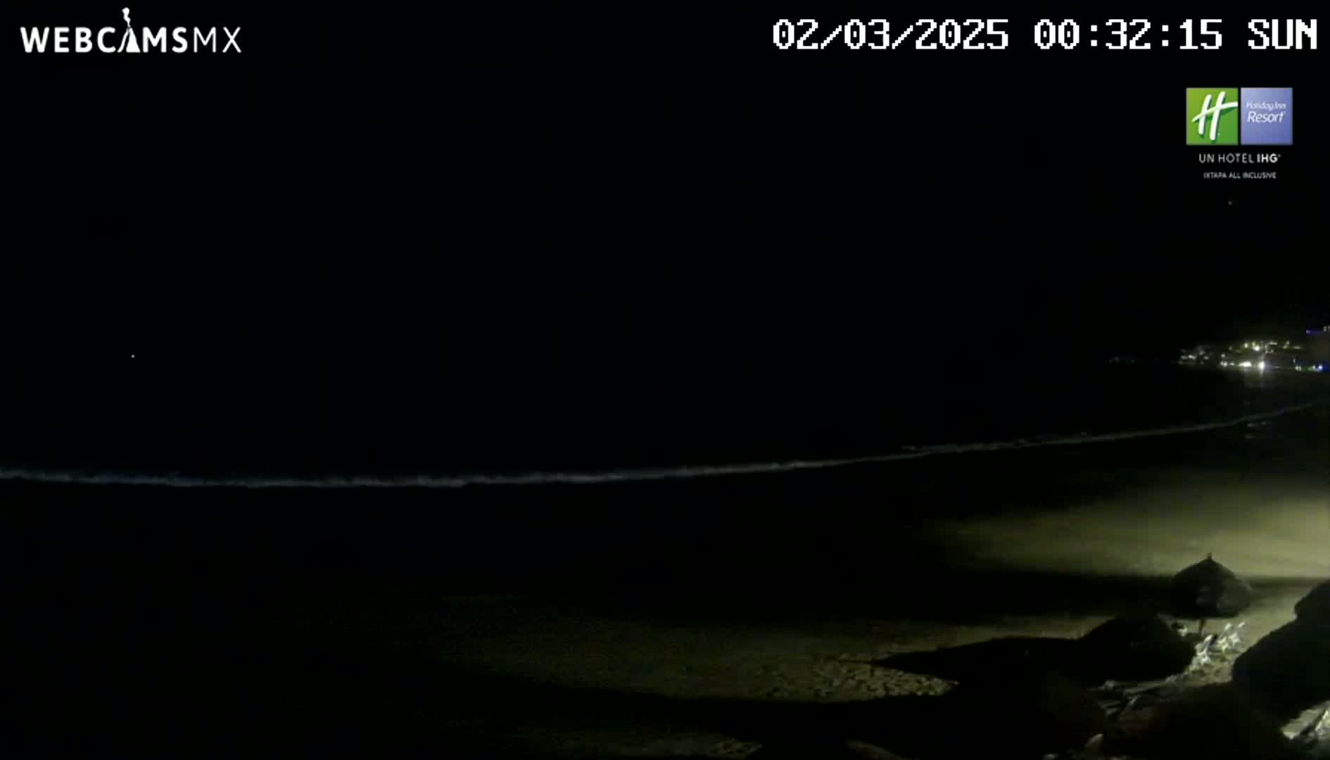 A dark, nighttime beach scene shows a gently lapping ocean under a clear, starless sky.