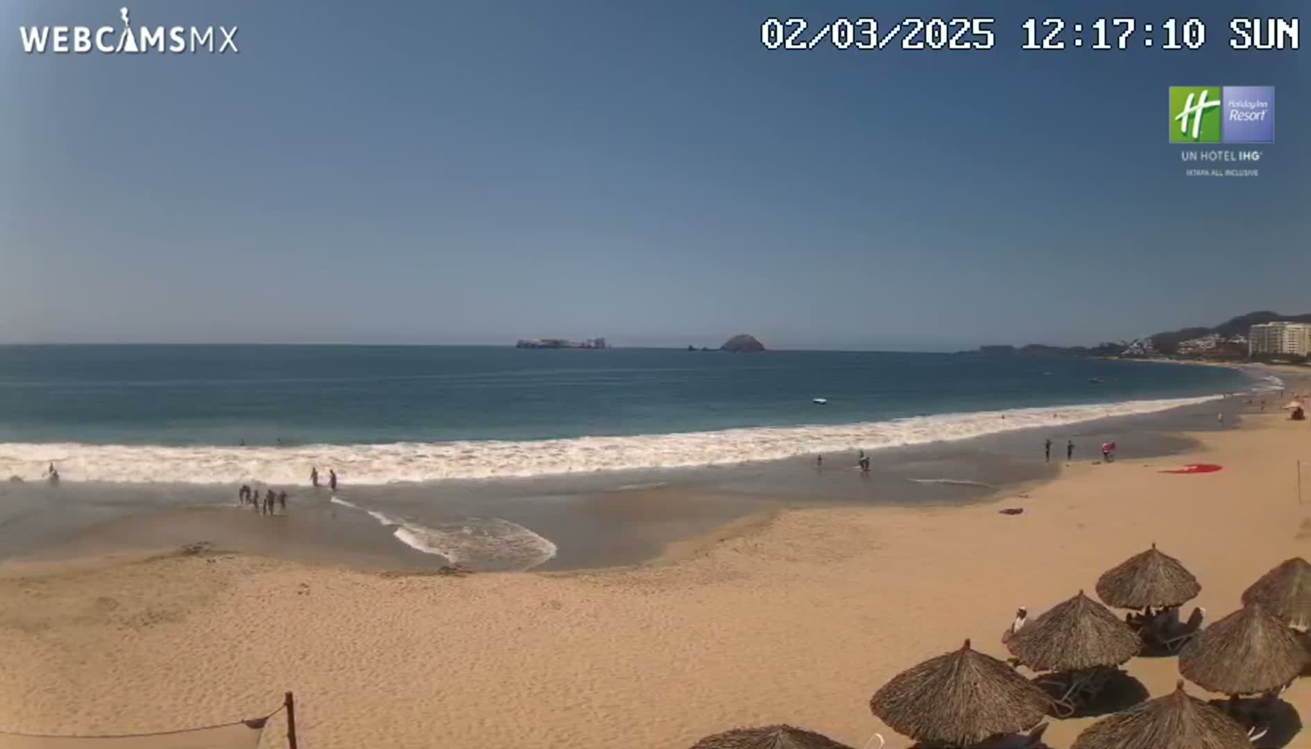 A sandy beach with gentle waves and a few people on a sunny day.