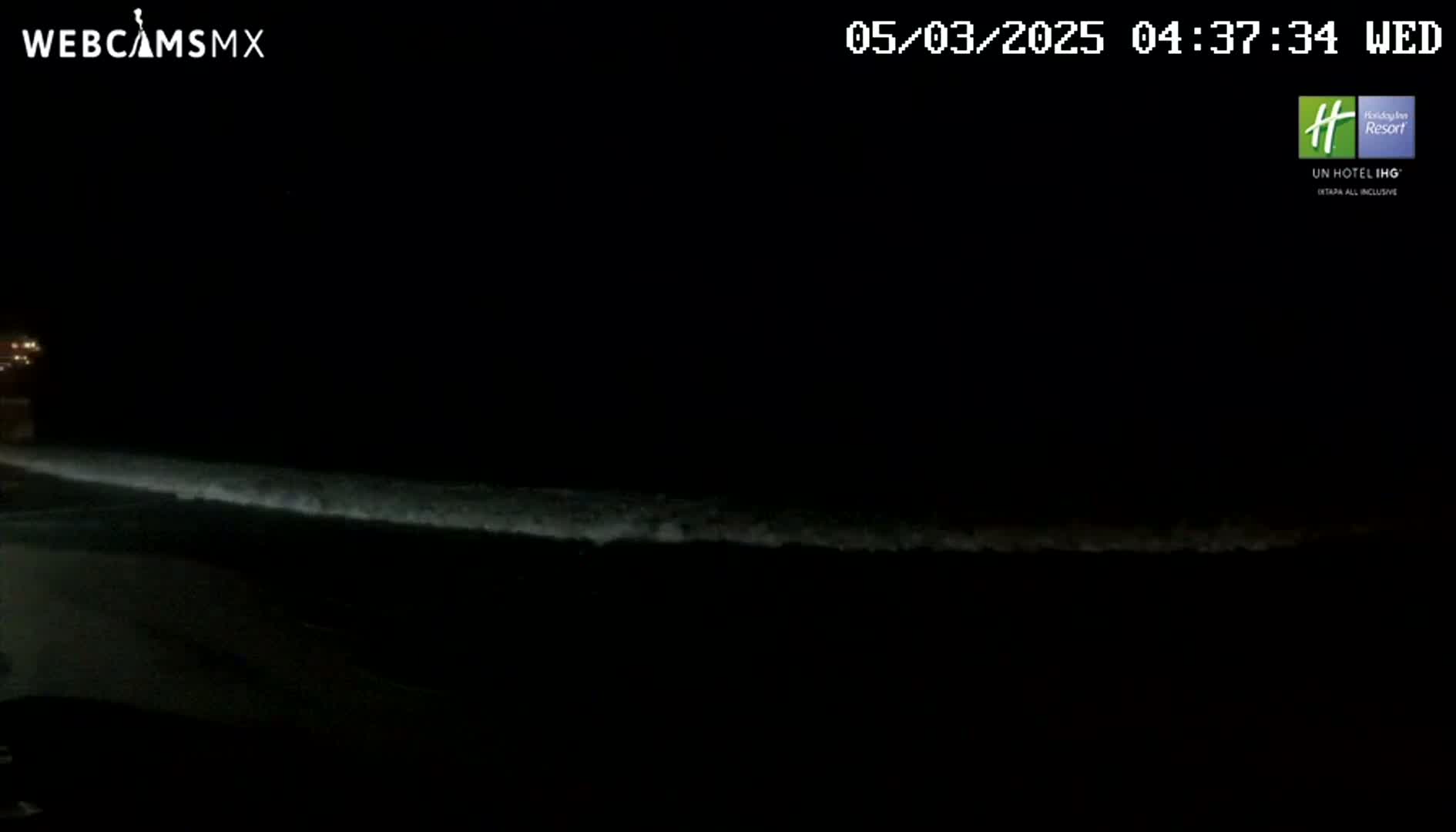 A dark beach at night shows a line of gently breaking waves under a clear, moonless sky.