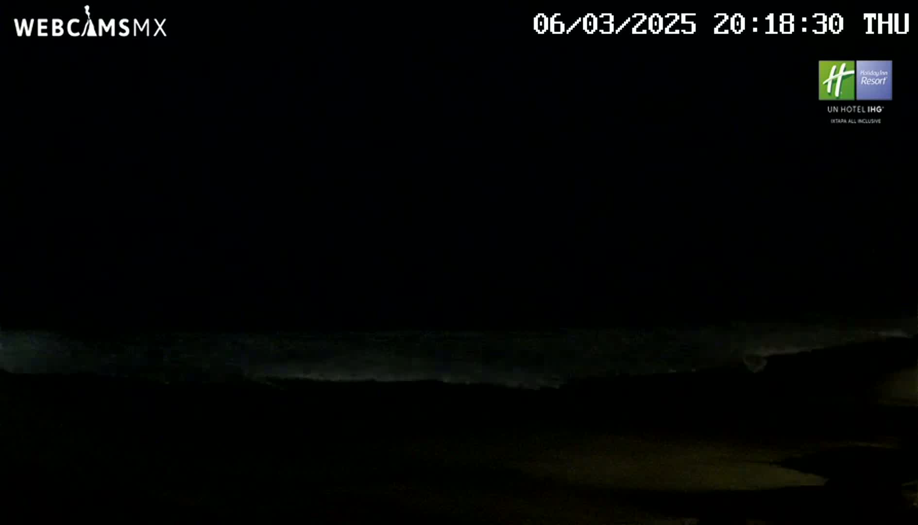 A dark nighttime scene shows ocean waves gently lapping the shore.