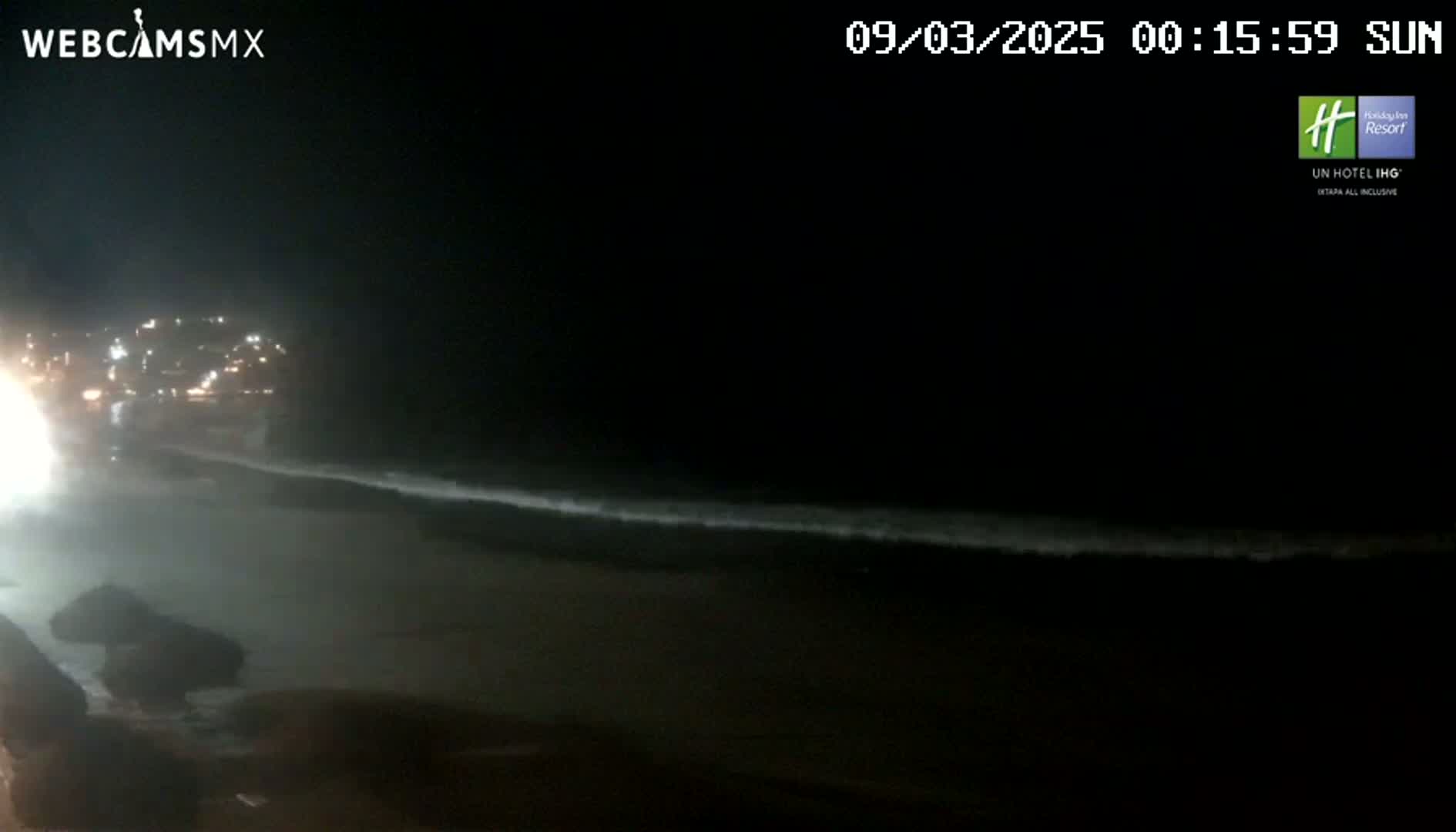 A nighttime beach scene shows dimly lit waves lapping the shore under a clear, dark sky.
