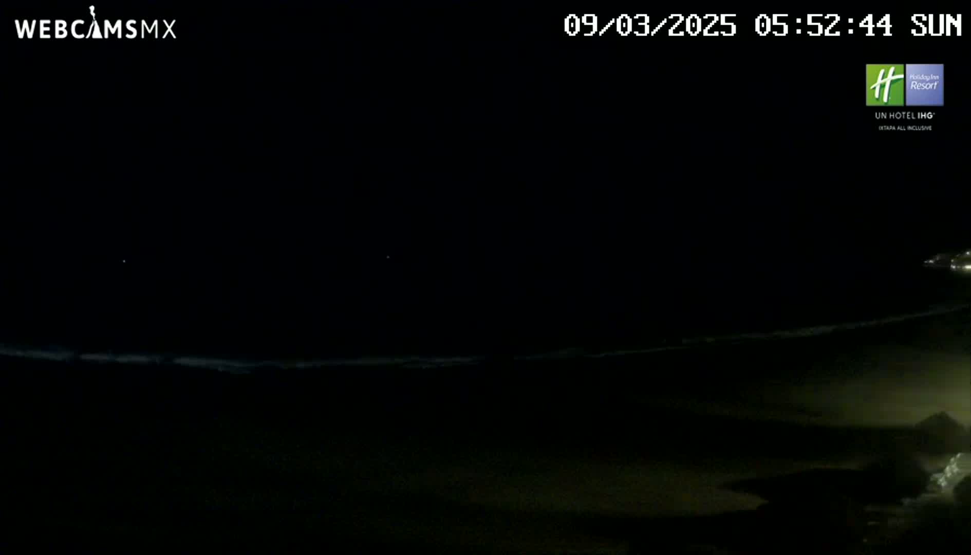 A dark nighttime beach scene shows a dimly lit ocean with waves lapping the shore.