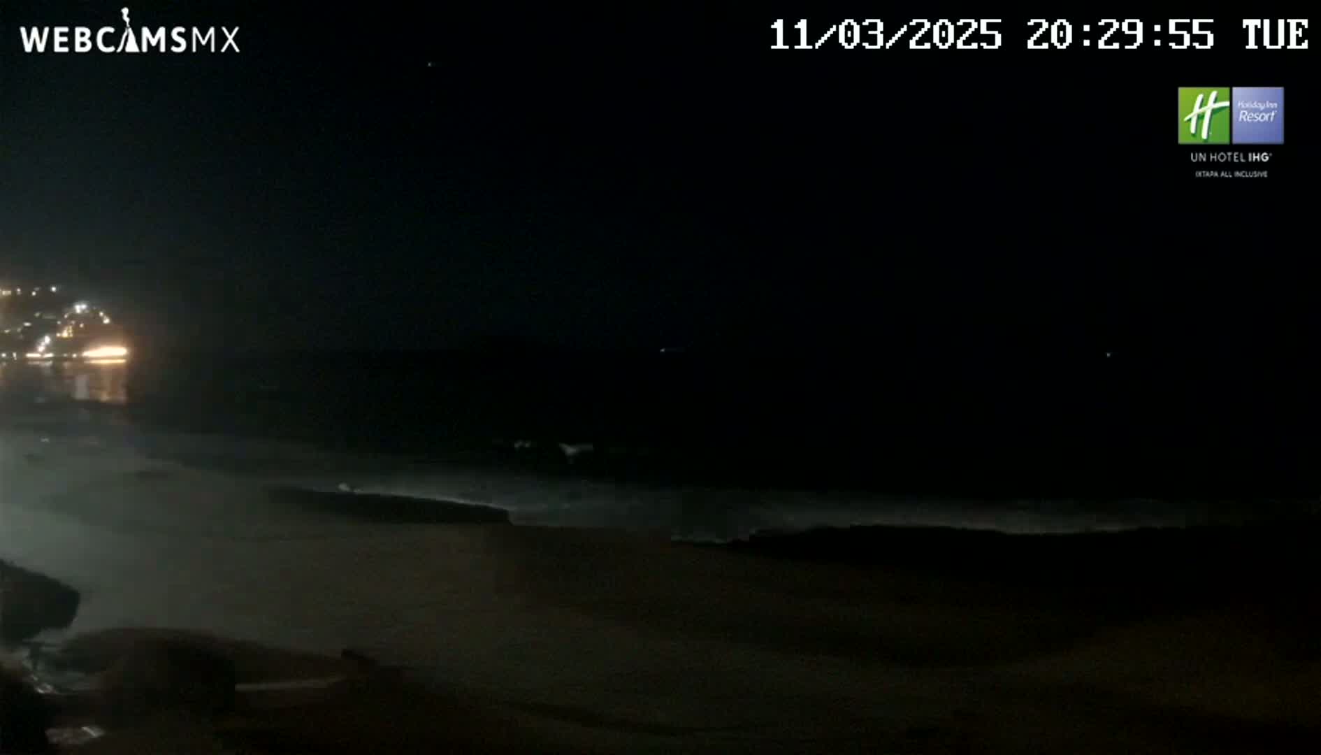 A dark nighttime beach scene shows a calm ocean with small waves lapping the shore under a clear, starlit sky.