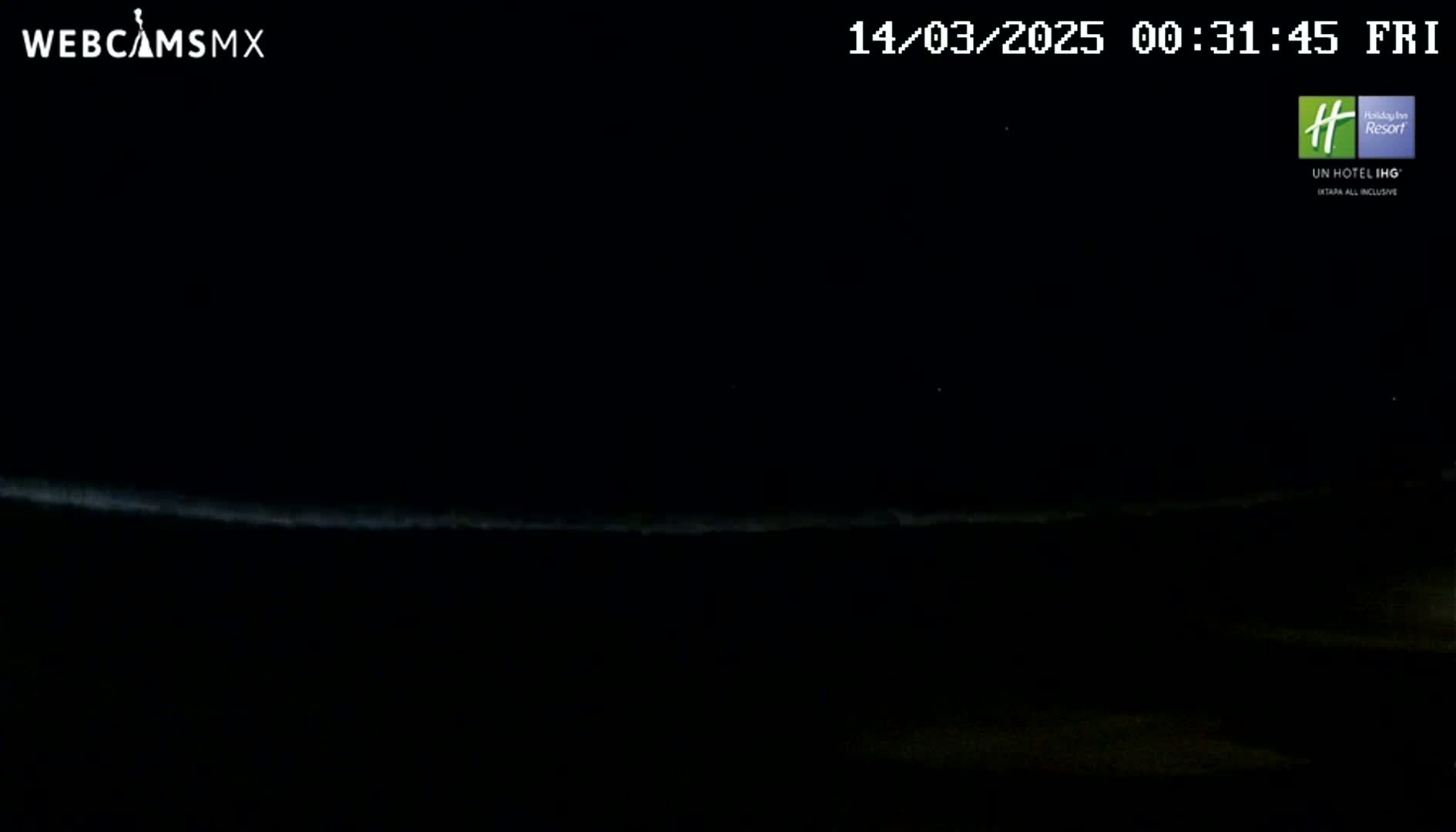 A nighttime, low-light view shows a faint, horizontal line of light on the horizon, possibly indicating the ocean or a distant light source.