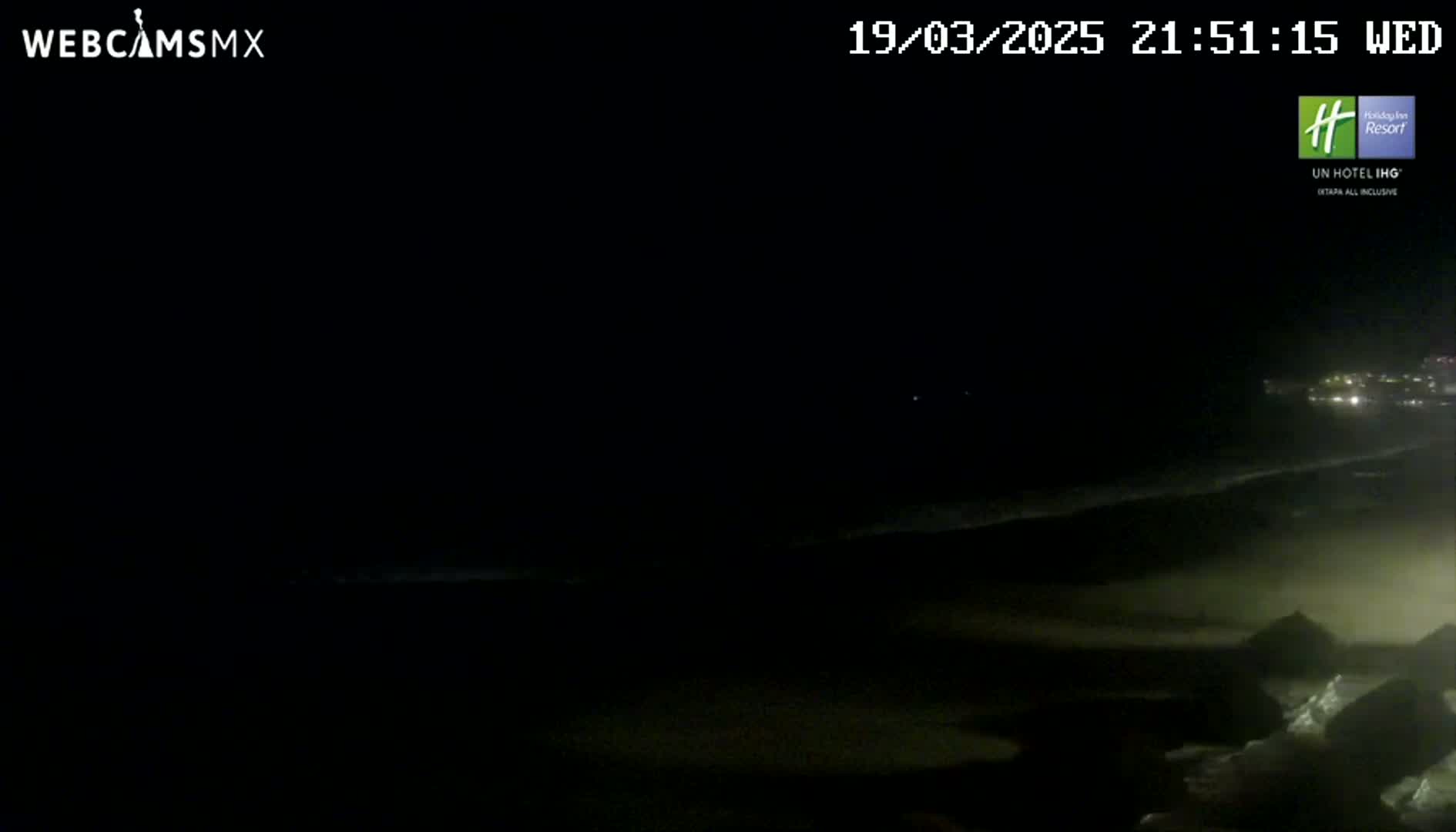 A dark, nighttime beach scene shows a dimly lit shoreline and ocean with faint waves under a clear sky.