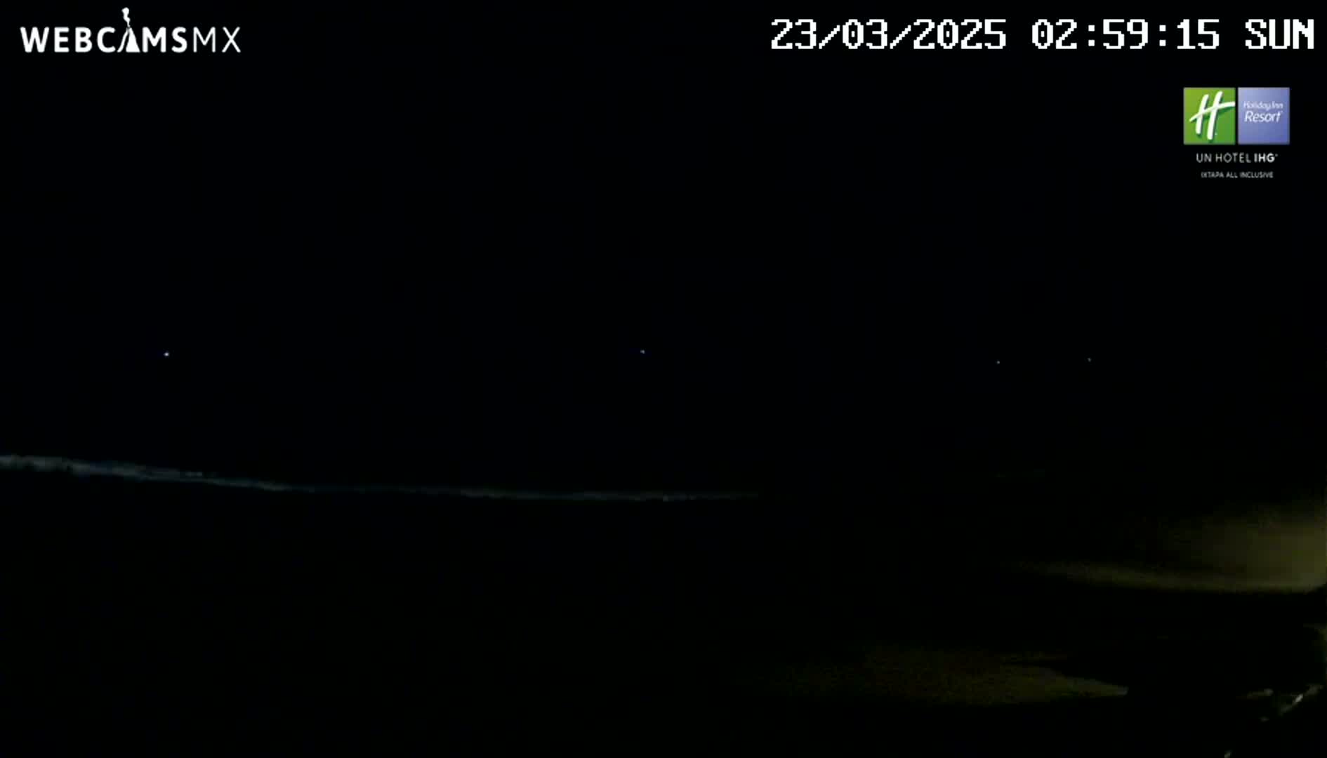 A dark nighttime scene shows a faint, light-colored horizon line and a few distant lights against a completely black sky.