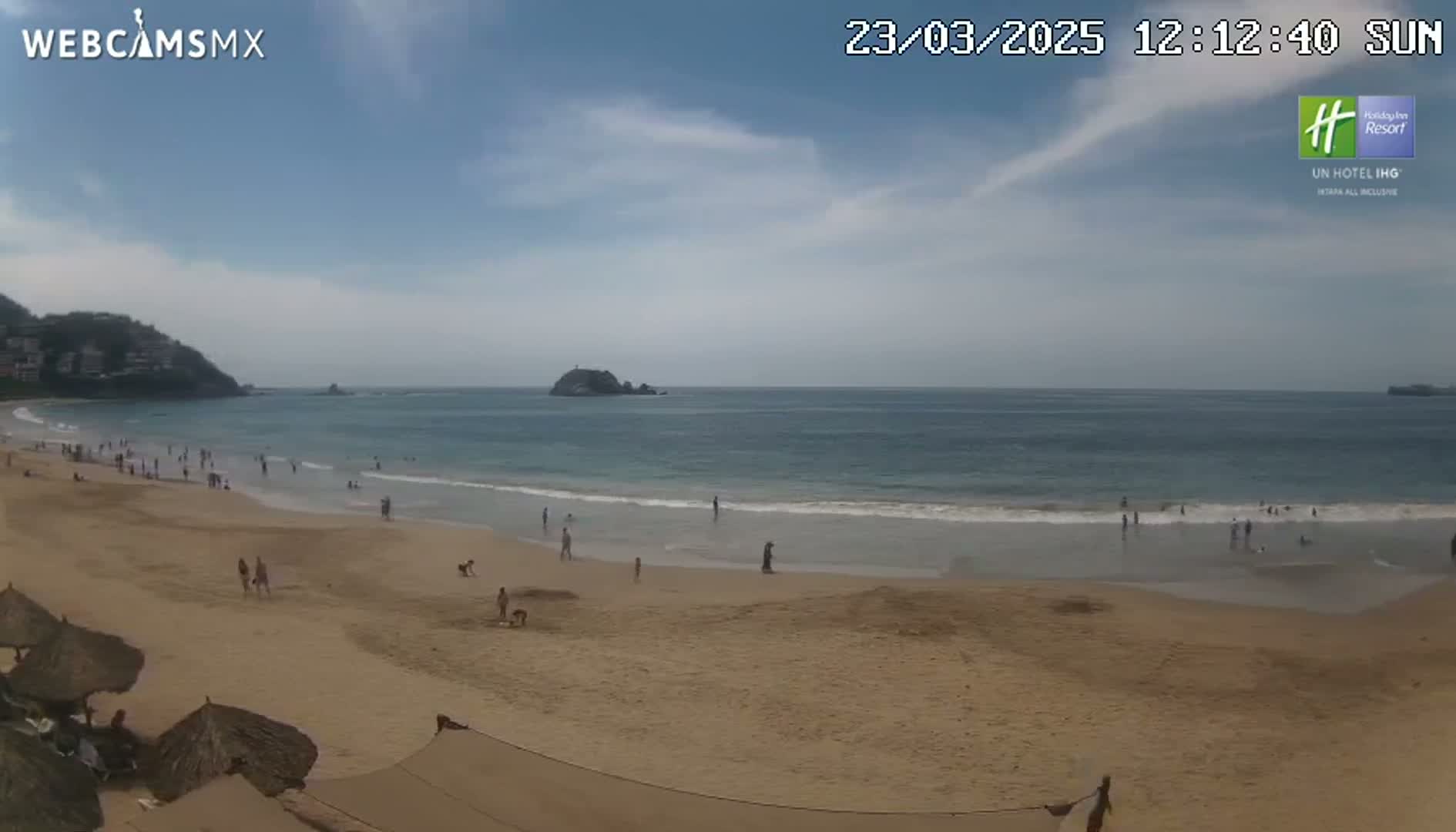 A mostly sunny day at a sandy beach with calm waves and scattered people enjoying the shore.