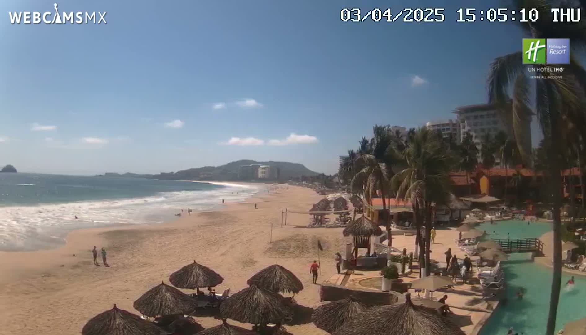 A sunny beach with light waves, palm trees, beach umbrellas, and a resort pool area is visible.