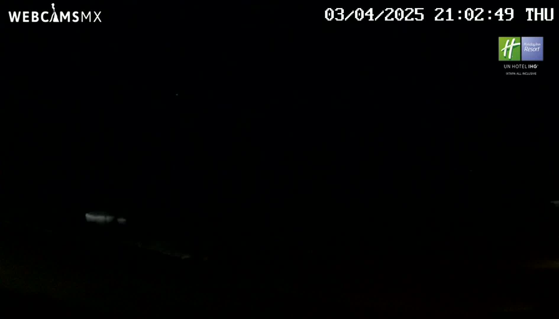 A nighttime image shows a dark, mostly featureless scene with a few faint lights visible in the distance.