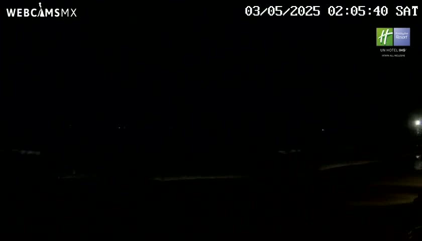 A dark, nighttime scene shows a dimly lit, flat expanse of land with a few faint lights in the distance.