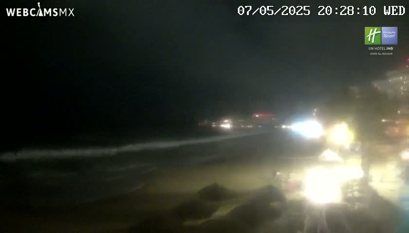 A nighttime beach scene shows gentle waves lapping the shore under a dark sky.