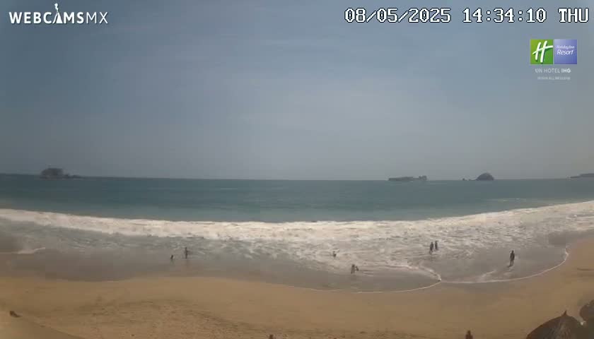A mostly sunny day at a beach shows light-colored sand, gentle waves, and a few people in the water and on the shore, with small islands visible in the distance.
