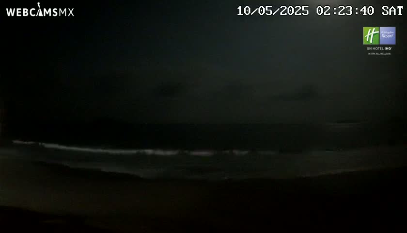 A dark, nighttime beach scene shows a calm ocean with small waves under a mostly clear sky.