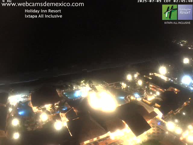 A brightly lit resort at night overlooks a dark ocean under a clear sky.