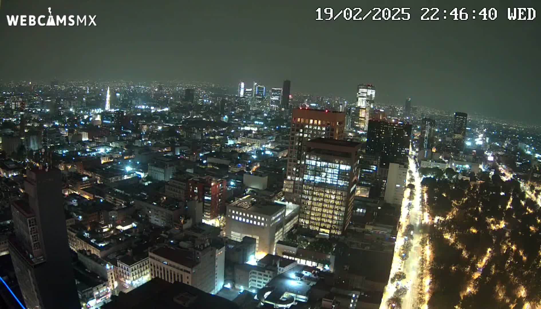 A nighttime aerial view of a densely populated city with illuminated buildings and streets, under a hazy sky.
