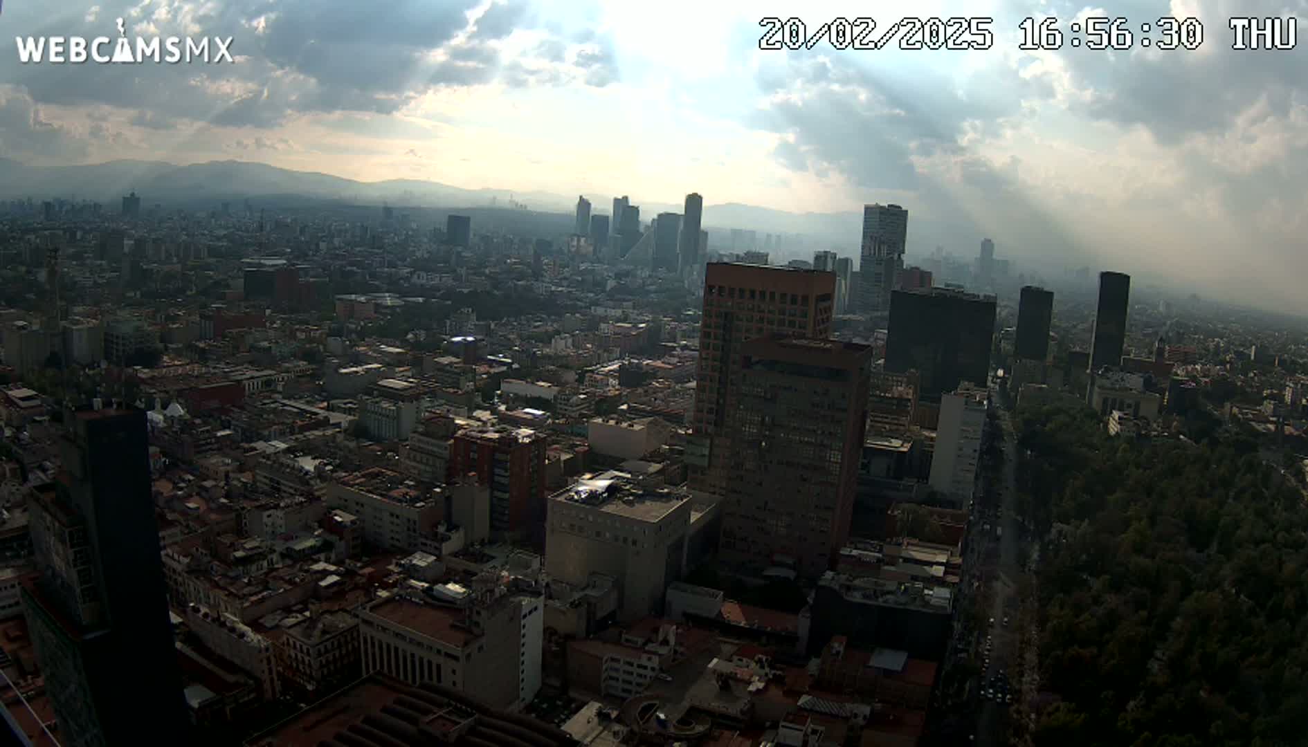 A hazy, partly cloudy day reveals a sprawling cityscape of densely packed buildings and skyscrapers, with a large park visible to the lower right.