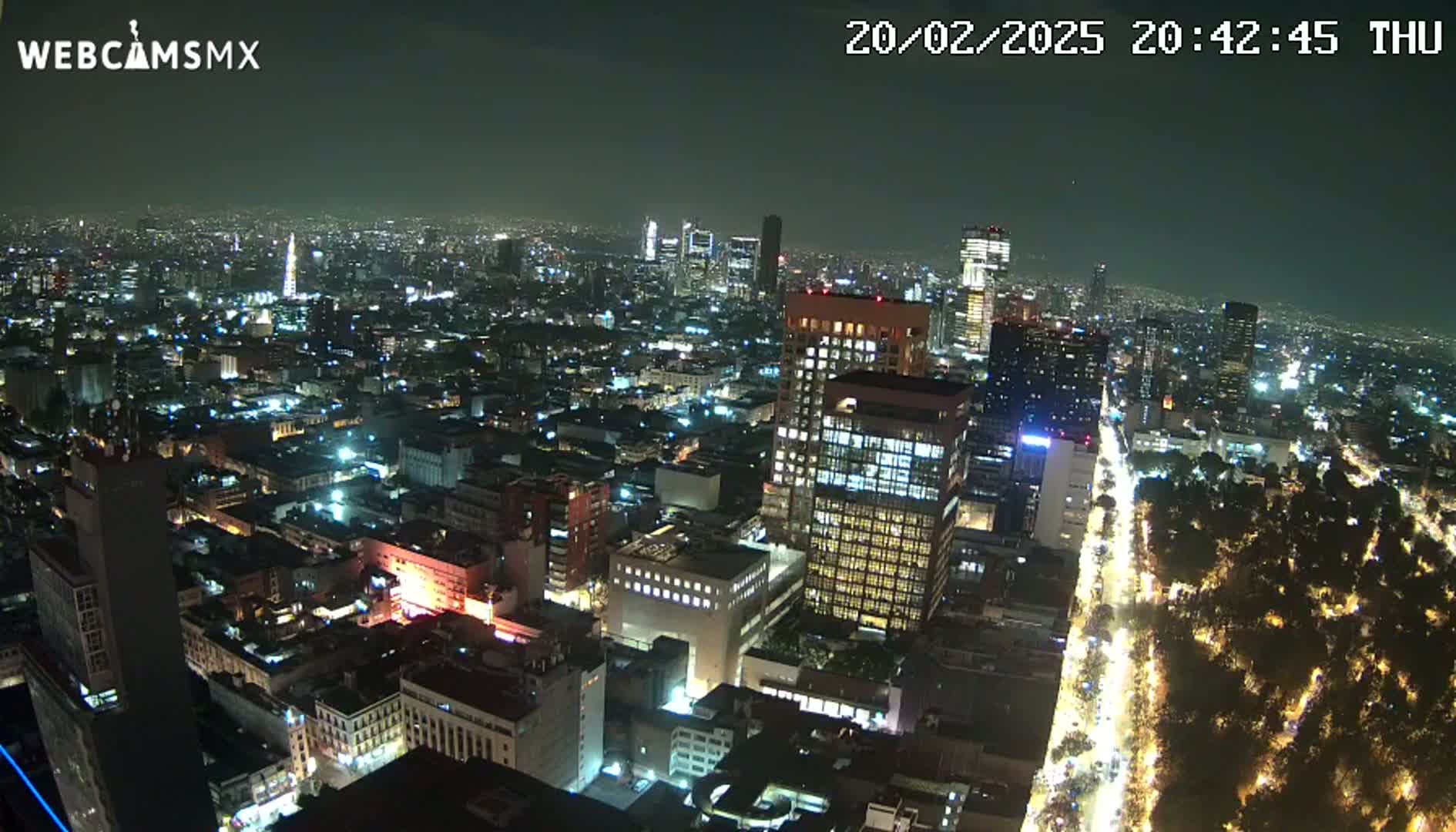 A nighttime aerial view of a large city with brightly lit buildings and streets, and a dark, clear sky.