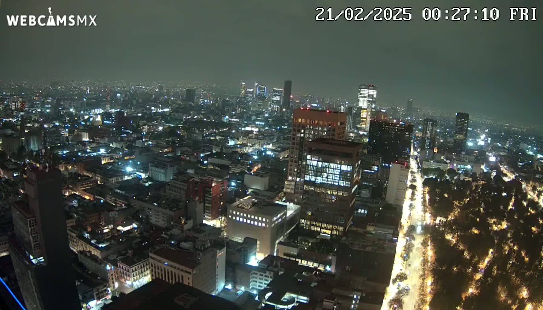 A nighttime aerial view of a densely populated city with brightly lit buildings and streets, under a hazy sky.