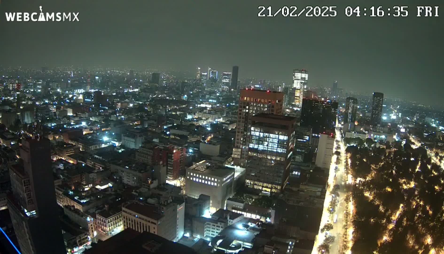 A nighttime aerial view of a sprawling city with numerous illuminated buildings and streets, under hazy or overcast skies.