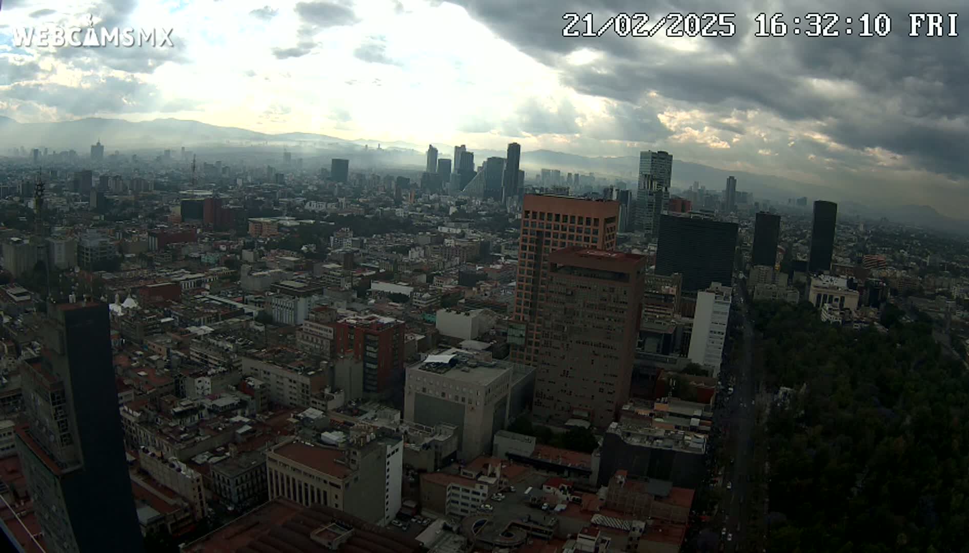 An aerial view of a sprawling city under a partly cloudy sky shows many buildings and a large park.