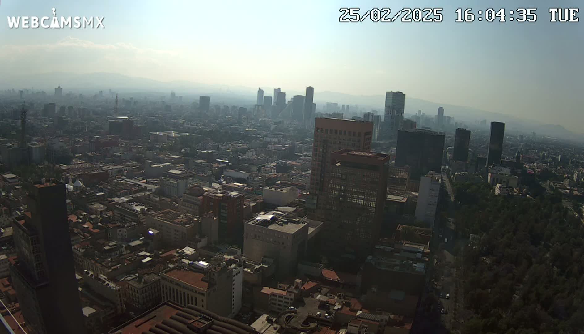 A hazy, high-angle view of a sprawling city with numerous buildings of varying heights, under a mostly clear sky.