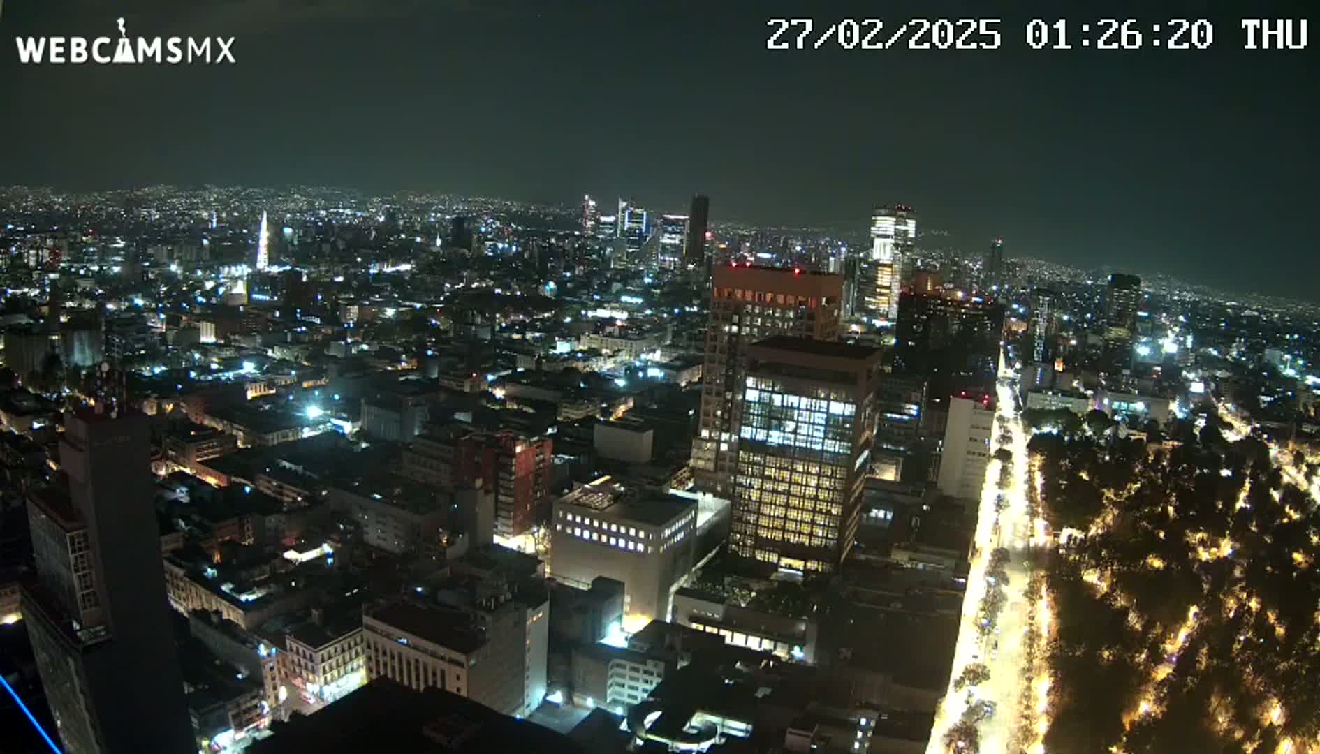A nighttime aerial view of a sprawling city with brightly lit buildings and streets, under a clear sky.