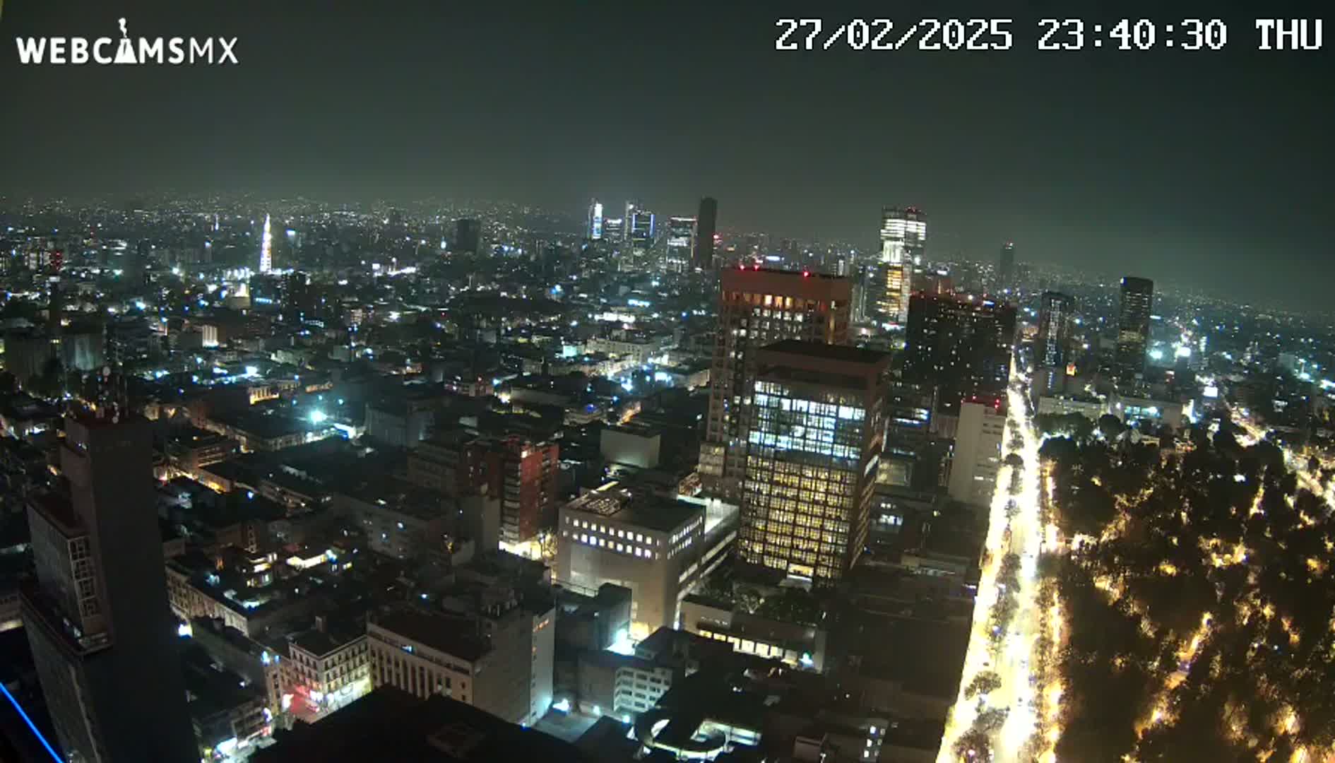 A nighttime aerial view of a sprawling city with brightly lit buildings and streets, under a dark, clear sky.