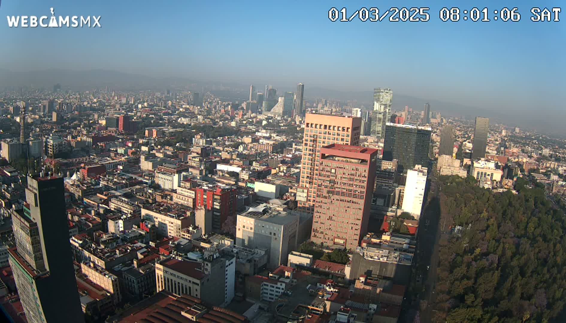 A hazy, sunny aerial view of a densely populated city with tall buildings and a large park.
