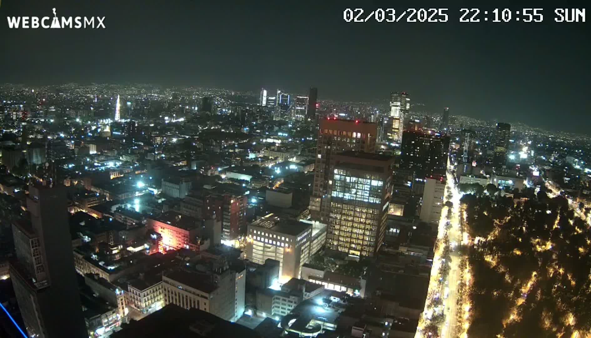 A nighttime aerial view of a large city with brightly lit buildings and streets, showing a wide expanse of urban development under a clear sky.