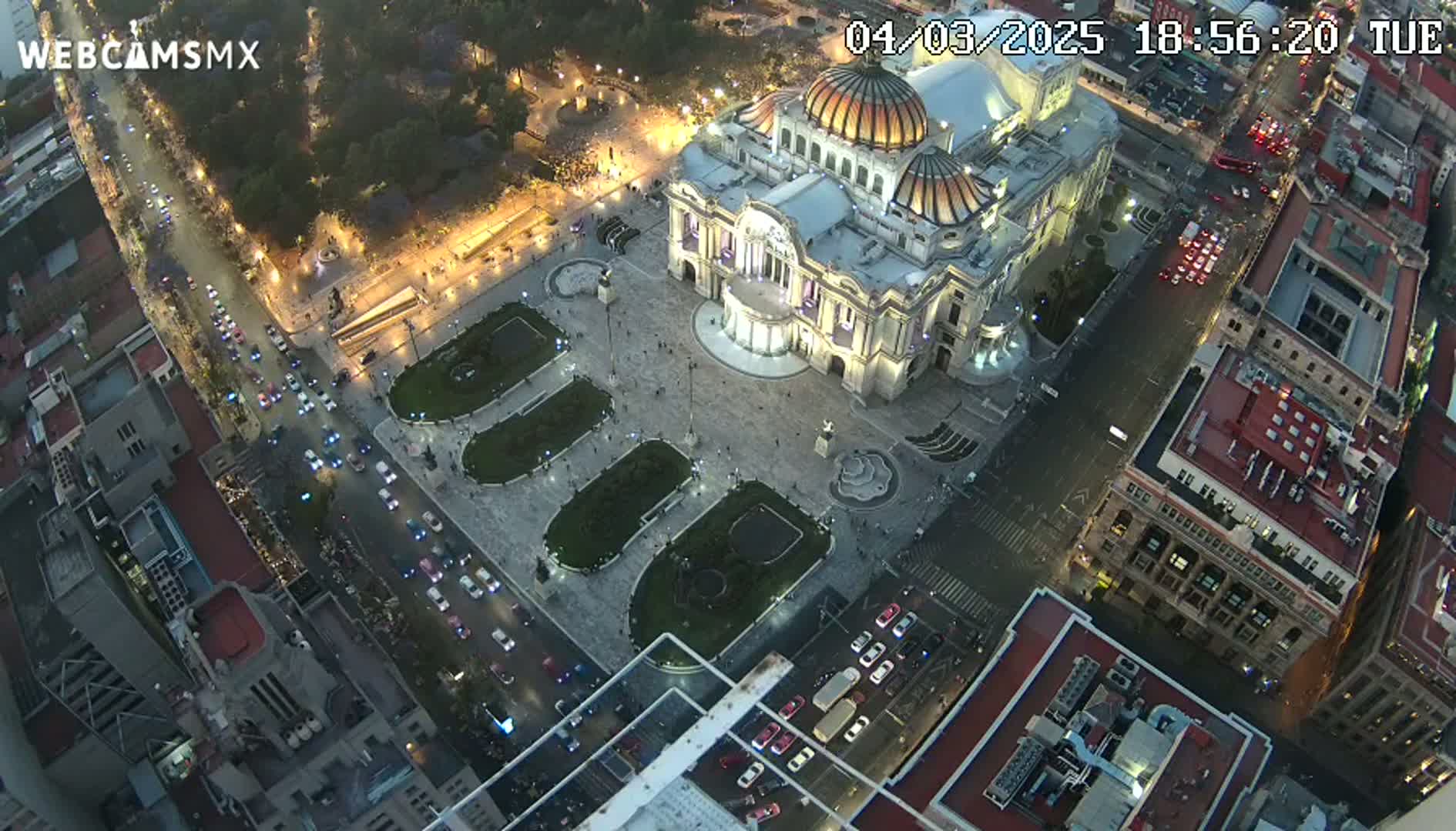 An aerial nighttime view of a large, ornate building situated in a city square with surrounding streets filled with cars, under a clear sky.