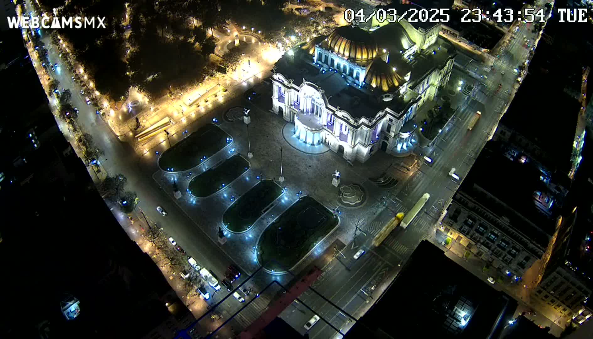 A brightly lit palace-like building sits in a plaza at night, surrounded by streets with minimal traffic.