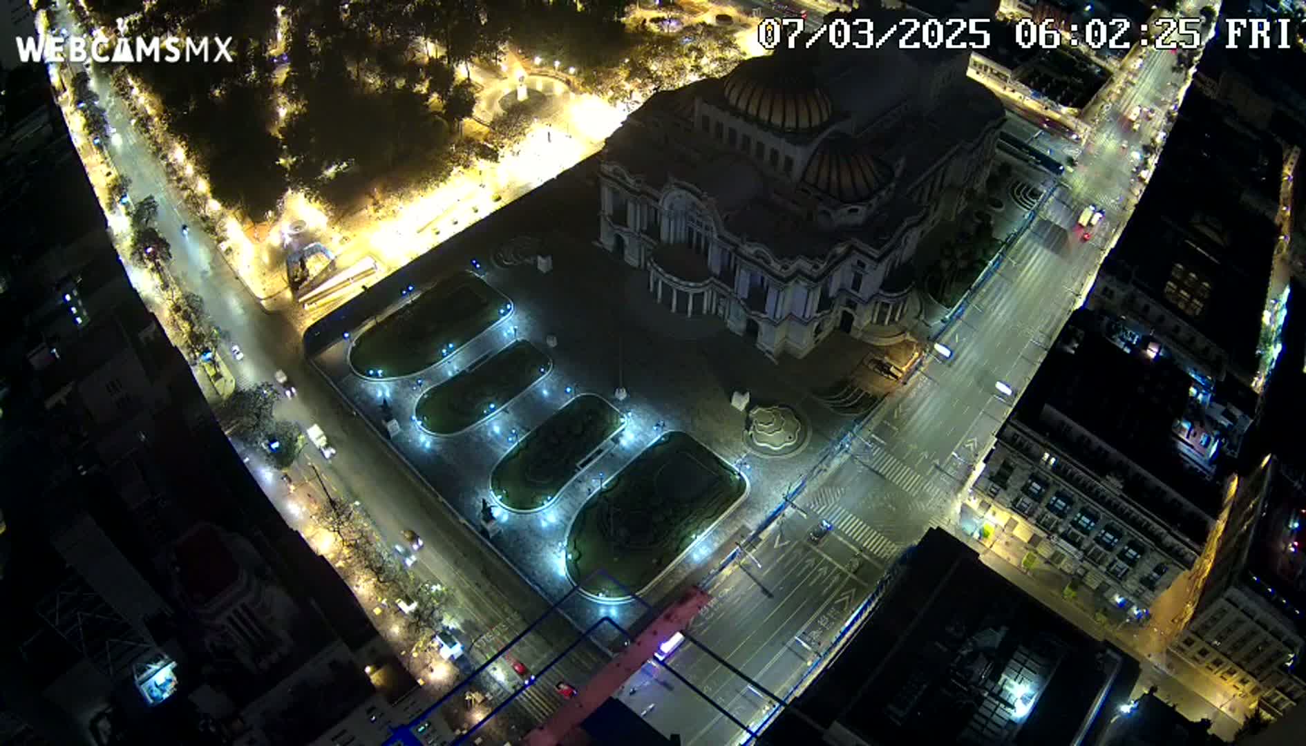 A nighttime aerial view shows a large building, illuminated streets with sparse traffic, and a plaza with landscaped areas.